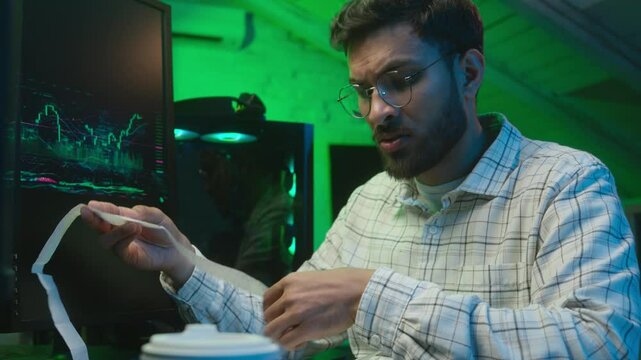 Frustrated Arabian Indian man programmer holding paper code bills problem checking information data monitor computer error mistake stressed male coder worried guy trader trouble IT worker lost office