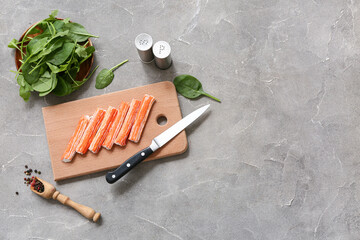 Wooden board with tasty crab sticks and spinach leaves on grey background © Pixel-Shot