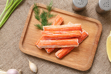 Wooden board with tasty crab sticks and dill on sack cloth background, closeup © Pixel-Shot