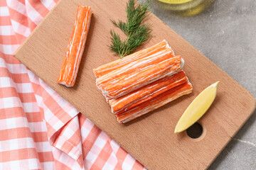Wooden board with tasty crab sticks, piece of lemon and dill on grey background © Pixel-Shot