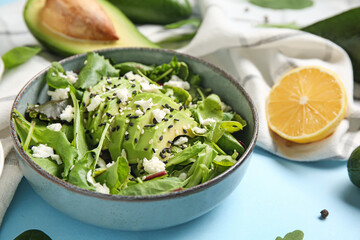 Bowl of tasty avocado salad with mozzarella cheese and lemon on blue background