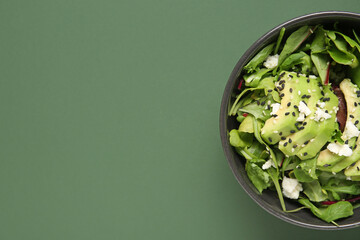 Bowl of tasty avocado salad with mozzarella cheese and sesame seeds on green background