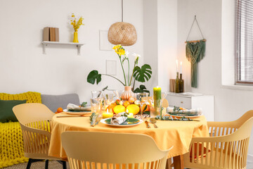 Festive table setting with citrus fruits, flowers and burning candles in room. Closeup