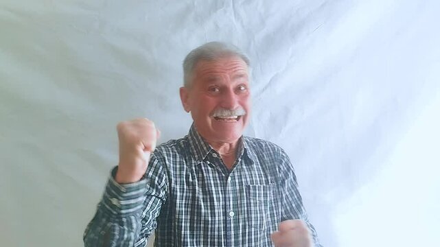 An elderly man in an enthusiastic mood comically expresses joy and looks at the camera.