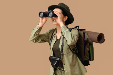 Young female tourist looking through binoculars on beige background