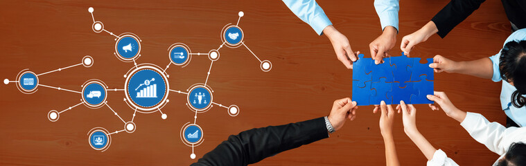 A diverse team collaborates to connect ideas on a blue puzzle piece, symbolizing business growth and innovation with digital connections on a wooden desk. Amity