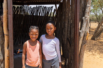 two village african girls with braids standing at the entrance of the outdoors kitchen, township...