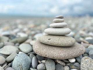 Stacked pebbles on pebbly beach with ocean background. Closeup of balanced pyramid stone stack on...