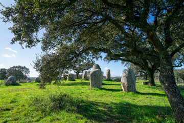 Ancient megalithic stones of the Cromeleque de Vale Maria do Meio in &Eacute;vora, Alentejo, Portugal, standing in a peaceful rural landscape under a blue sky.