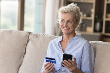 Easy online paying. Portrait smiling senior woman ecommerce shopper e bank client sitting on sofa...