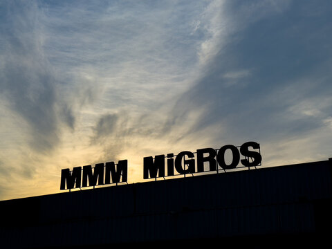 MMM Migros sign silhouetted against a sunset sky in Turkey. Migros supermarket logo at dusk with colorful clouds. Biggest chains. Turkish retail landmark. Samsun, Turkey - Oct 29, 2023