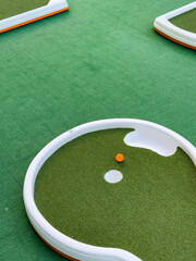 Mini golf course with hole, orange ball on green turf and white borders. Playful recreation, casual sport and enjoyable activities concept 
