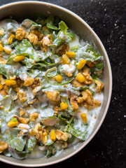 Creamy purslane salad with greens, corn, and walnuts in beige bowl. Round bowl of healthy purslane salad with dressing. Fresh ingredients, healthy eating and nutrition concept