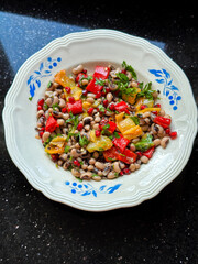 Colorful black bean salad with roasted peppers, herbs, and pomegranate on decorative plate. Fresh mediterranean black eyed pea salad. Healthy eating, nutrition and wholesome meals concept