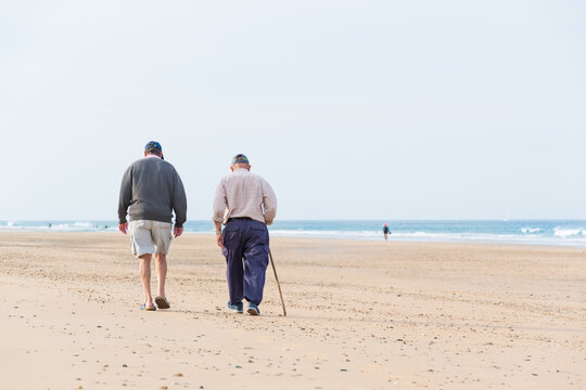 An older, retired couple walking along the beach sand. A scene with waves and nature