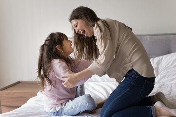 Carefree play. Overjoyed candid young single mother little daughter having fun playing tickling...