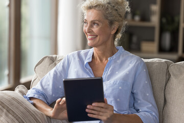Pause for thought with digital device. Dreamy pensive aged woman retiree sitting on couch looking aside of tablet reflect on convenience of ecommerce shopping inspired by new idea from social media