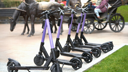 Renting electric scooters in Kislovodsk.  Accumulation of vehicles on the blurred background of the pedestrian street with a sculpture of a bronze horse-drawn carriage .