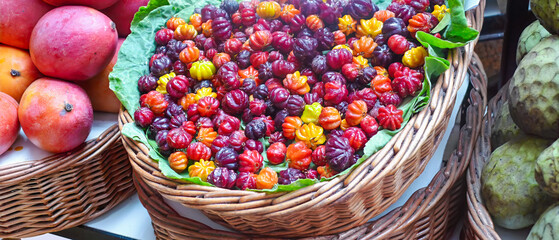 Pimenta da Madeira peppers on market, vibrant red orange yellow purple peppers, wicker basket with green leaves, tropical market scene. For culinary ingredients, tropical taste, copy space.
