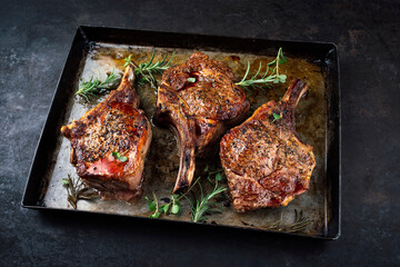 Traditional barbecue dry aged veal chops with Mediterranean rosemary and spice served as close-up in a rustic backing form on a black board