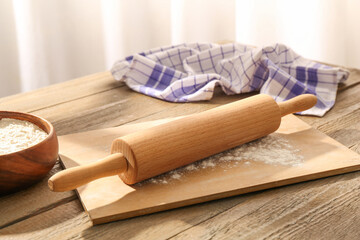 Rolling pin, flour, board and napkin on wooden table indoors, closeup