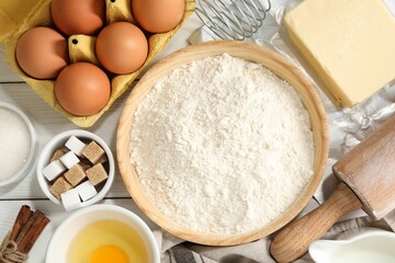 Rolling pin and ingredients for dough on white wooden table, flat lay