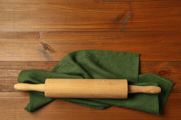 Rolling pin and green napkin on wooden table, top view. Space for text