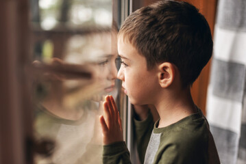 The child looks at the street through the glass of the door. Emotions