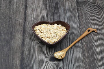 Oatmeal flakes and oats on a heart shaped plate on black background. Healthy breakfast. Organic and vegetarian food.