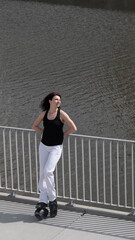 Fototapeta premium A woman jumps energetically on kangaroo boots by the riverside, embracing outdoor fitness with a smile. The blend of innovative exercise gear and urban scenery showcases the evolution of modern