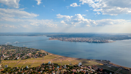 Aerial view showcasing a portion of Encarnación city, Paraguay, with the Paraná River and a broader view of Posadas city, Argentina, in the distance.