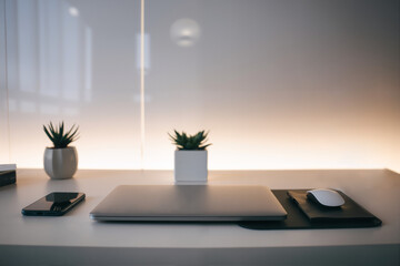 Minimalist home office with a closed laptop, smartphone, and a small potted plant on the table — space for text. This image was created using AI technology.
