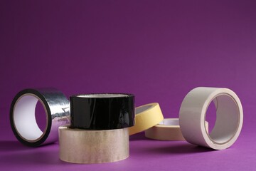 Rolls of different adhesive tapes on purple background