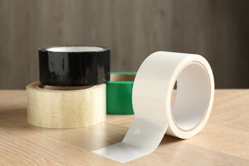 Rolls of different adhesive tapes on wooden table, closeup