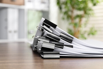 Binder clips with sheets of paper on wooden table indoors, closeup