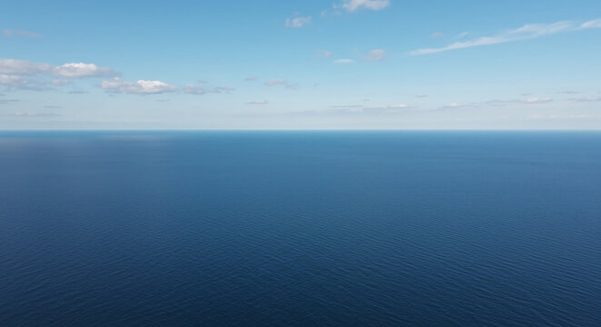 Aerial view of a calm blue ocean under a bright blue sky with a few scattered white clouds above it