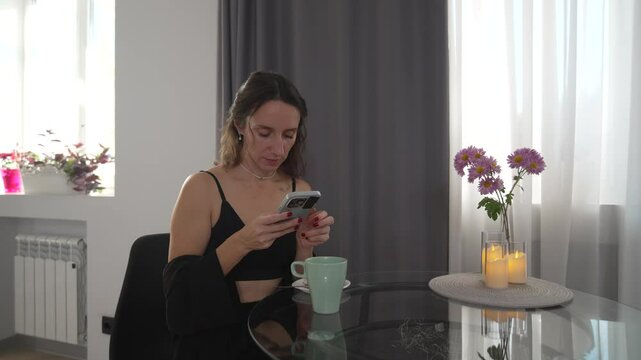 Woman Smartphone Home, morning: Lady texts at table with flowers, candles, enjoying leisure time indoors.