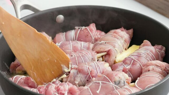 cook put piece of butter on resh raw chicken thighs meat filled rolls frying on pan, process of making healthy meal, food closeup