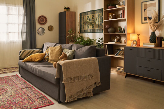 Living room interior showcasing eclectic mix of bohemian decor with cozy couch, patterned rug, and shelf of books. Soft lighting from lamp creating warm and inviting atmosphere