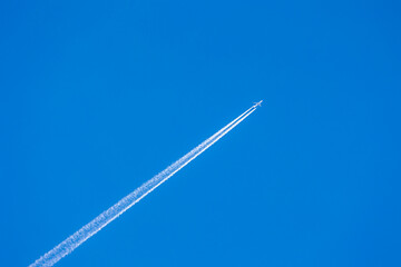 Airplane and contrails or vapour trails after a large commercial jet plane high in sky, Diagonal trace of plane flying in clear blue sky, Aircraft waste smoke trails, Air transport background.