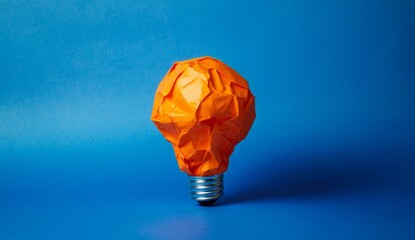 Crumpled orange paper lightbulb on blue background;  failed idea concept