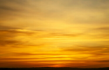 Golden hour sky with soft clouds and a dark horizon line in a warm and vibrant color palette