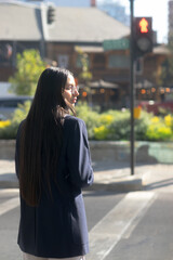Fototapeta premium Young Hispanic businesswoman with blue blazer, white shirt, looking at stopped cars – Red traffic light in the background
