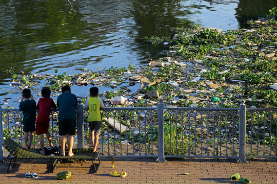 Children looks on the big amount of trash polluting the water of Saigon river in Ho Chi Minh City, Vietnam.