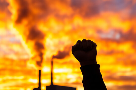 Raised fist protest silhouette against industrial pollution and vibrant sunset sky — environmental activism concept