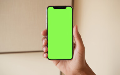 Person holding modern smartphone with green chroma key screen in indoor setting for app design or digital mockup
