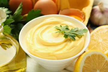 Delicious mayonnaise sauce with parsley in bowl and ingredients on white table, closeup