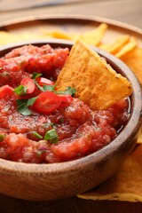 Delicious spicy salsa sauce with nacho chip in bowl on table, closeup