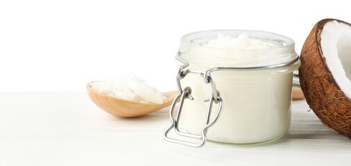 Organic coconut cooking oil in jar, spoon and fresh fruit on wooden table against white background