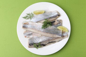Marinated herring fillets with lime and dill on green background, top view